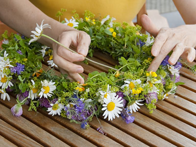 Frauenhände flechten einen Kranz aus Wildblumen